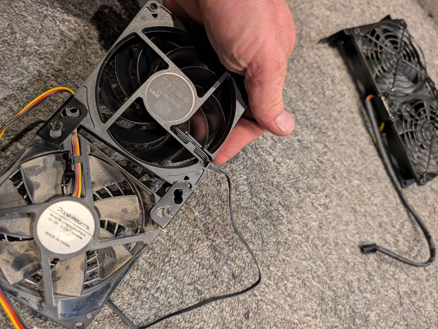 Two 92 mm fans on the carpet: a dusty Pano-mounts fan taken out of the bracket and a black Cooler Master SickleFlow 92, with the bracket beside them.