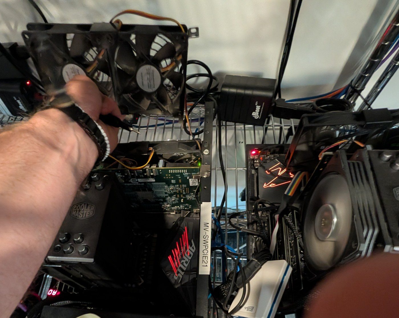 A hand lifting a two-fan bracket from a frame on the lab shelf labelled MV-SWPCIE21.