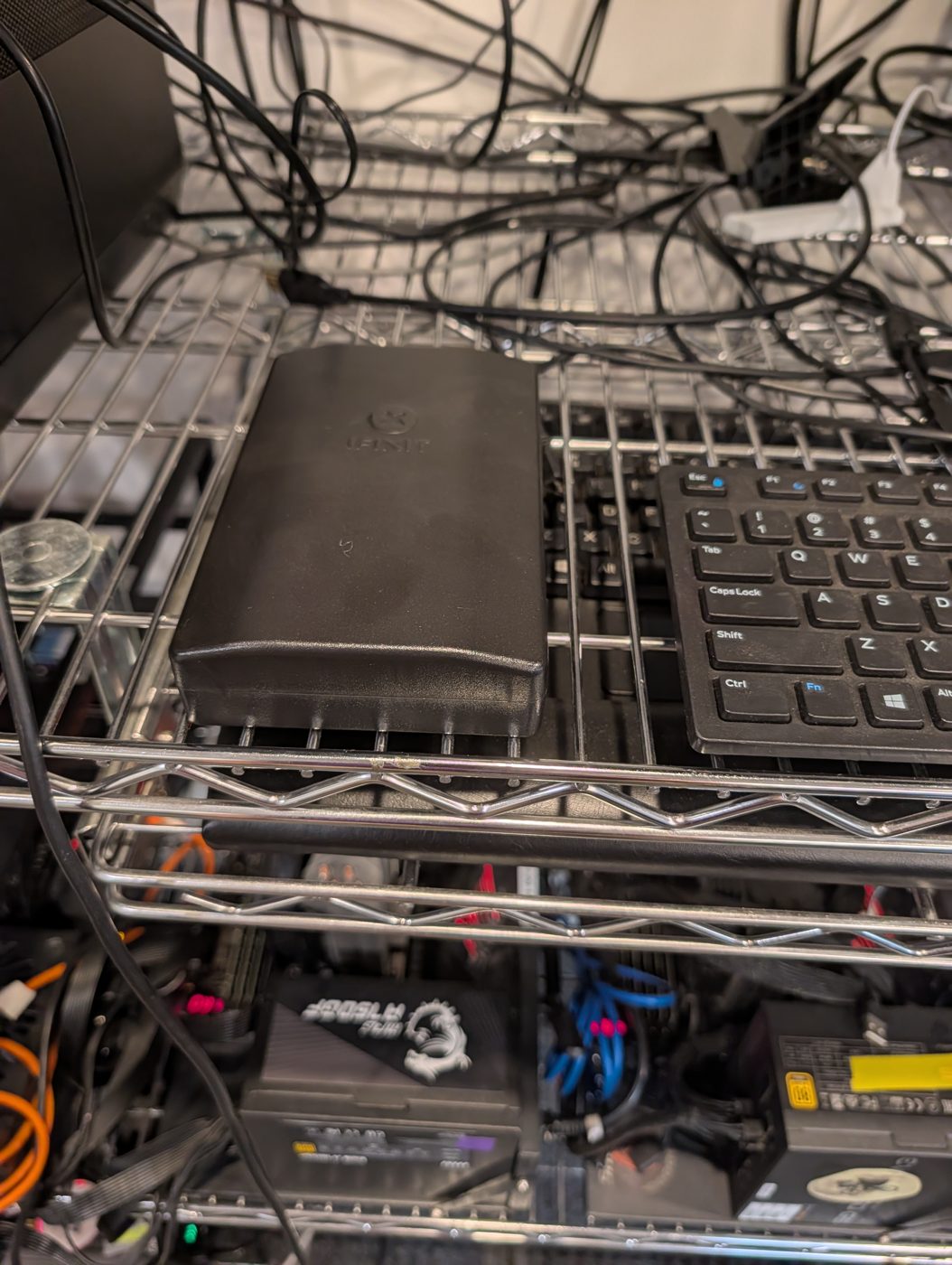 A black toolkit case on the wire shelf beside a keyboard, above the lab machines.